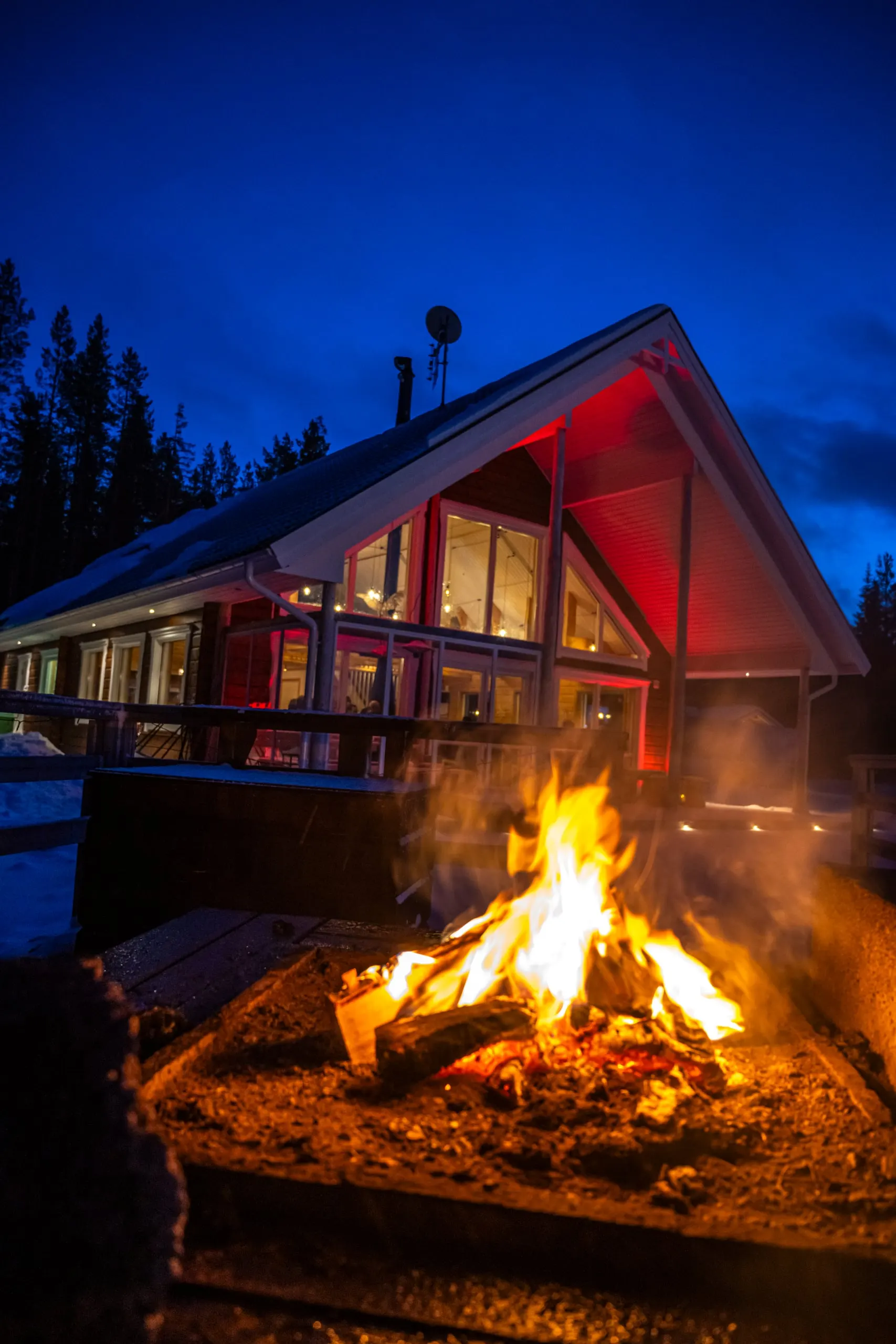Lagerfeuer vor einer beleuchteten Hütte in der blauen Stunde