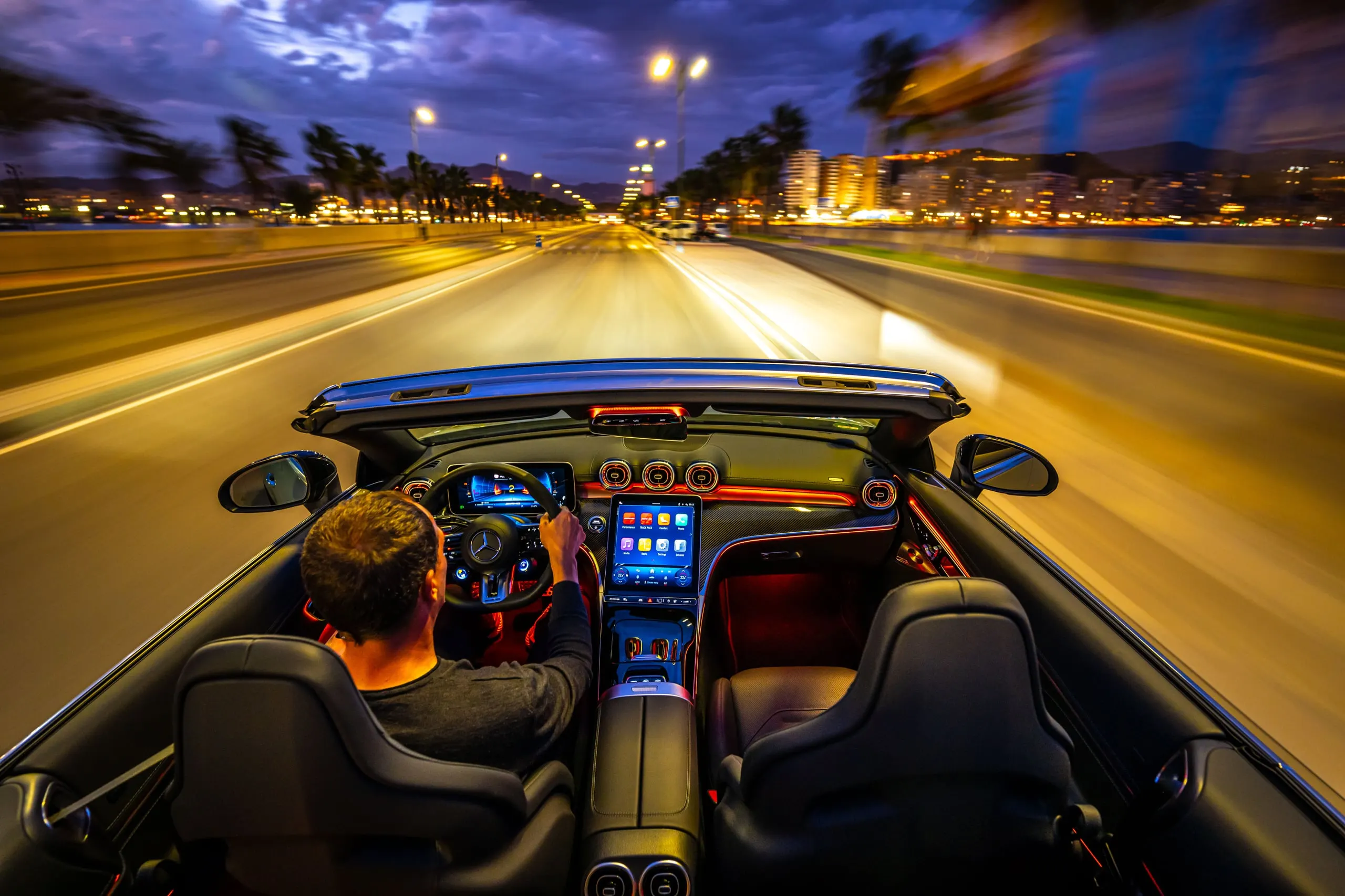 Blick über den Fahrer auf eine beleuchtete Straße bei Nacht