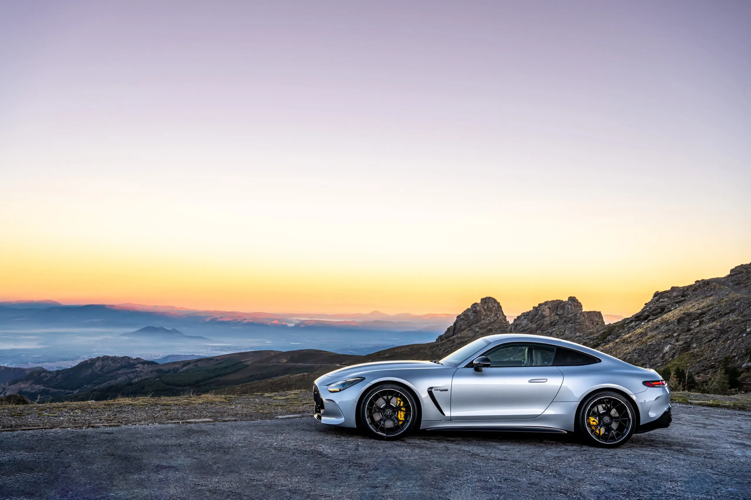 Silberner AMG GT in Seitenansicht vor Abendhimmel über den Bergen