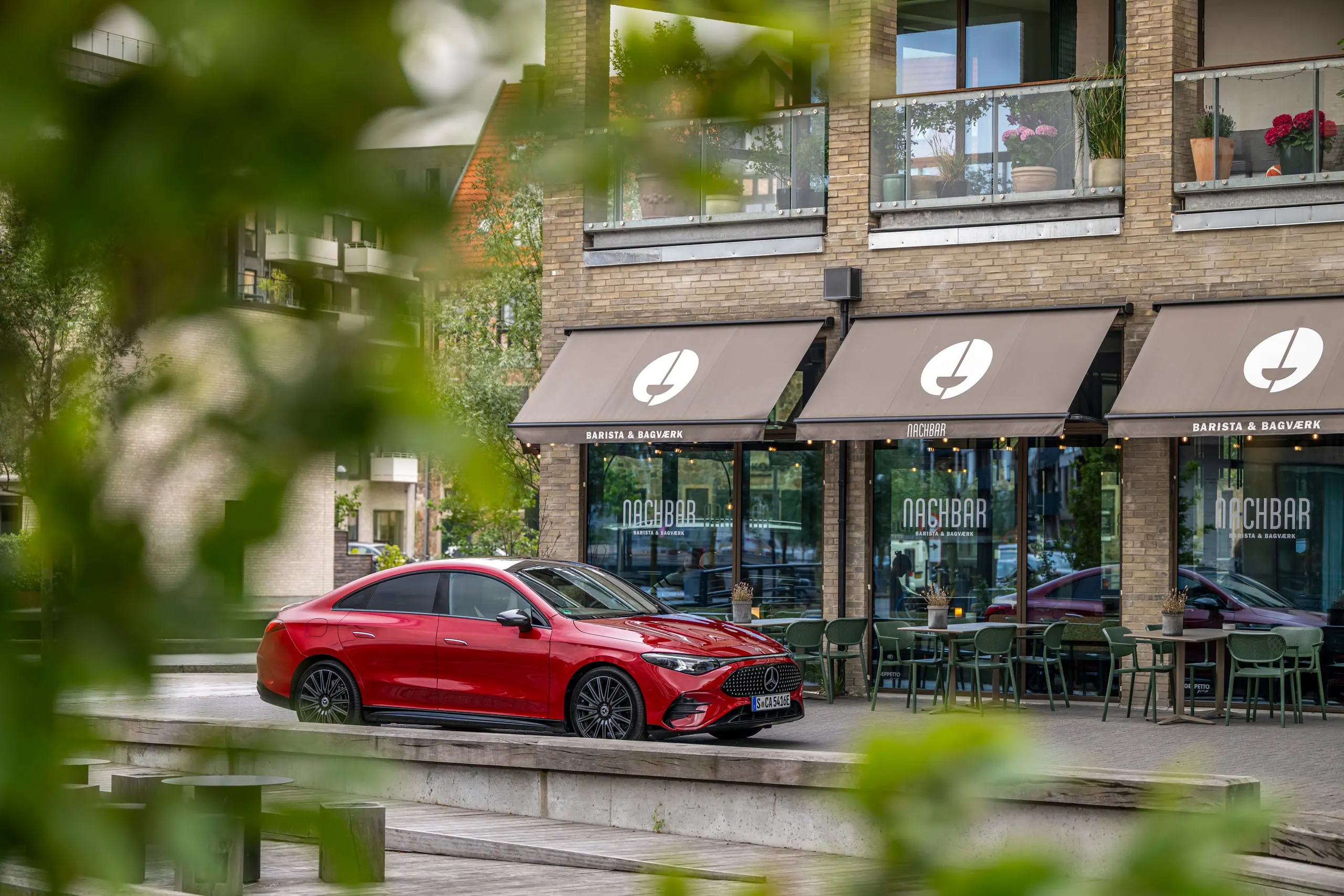 Roter CLA durch Blätter vor einem Café fotografiert
